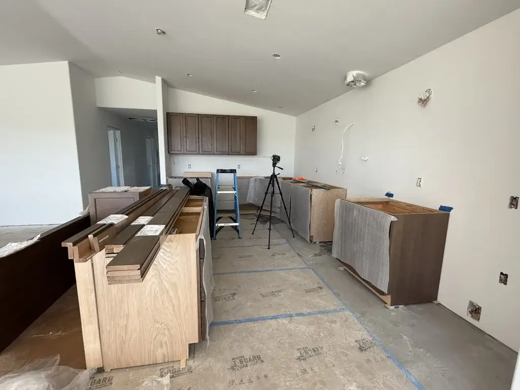 Kitchen cabinet boxes set in place mid-installation, with trim stacked and electrical outlets roughed in